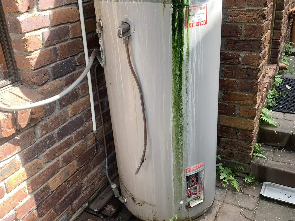 Before — a rusted, mossy electric hot water system swapped for a new Vulcan unit with tidy new pipework