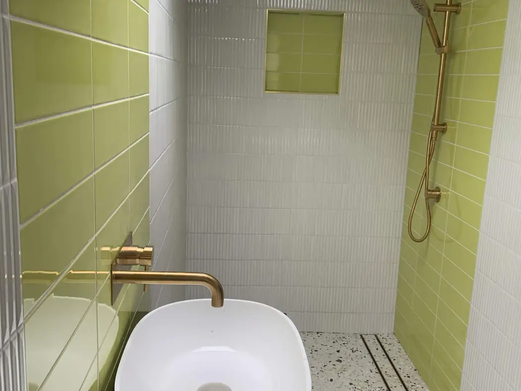a finished bathroom with brass tapware, rain shower and a linear floor drain